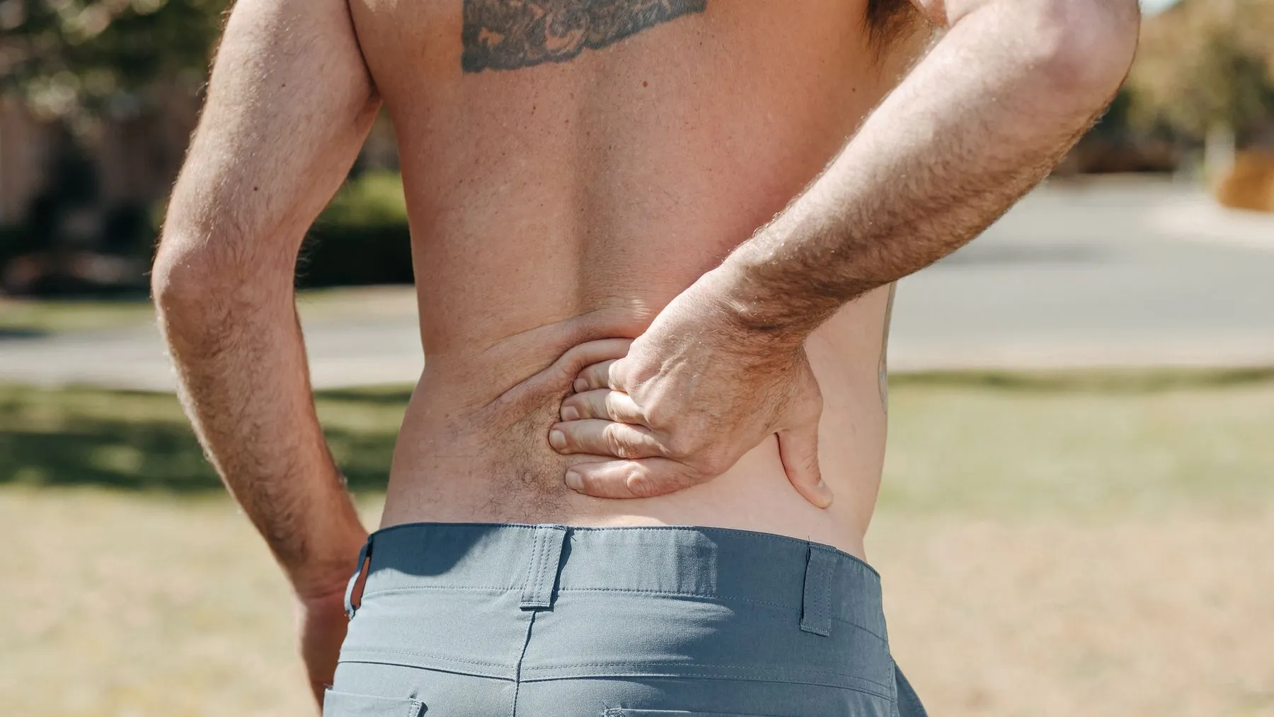 A man holding his lower back with one hand, the spot a back decompression device is meant to relieve