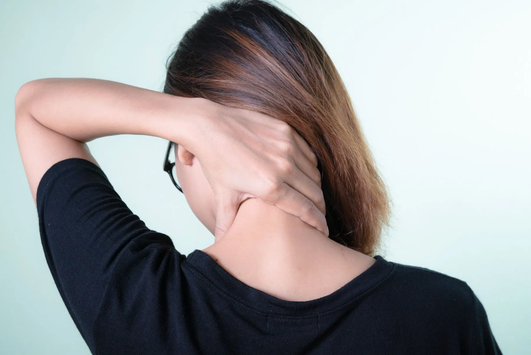 A woman seen from behind holding the back of her neck, the kind of stiffness a neck stretcher is bought for