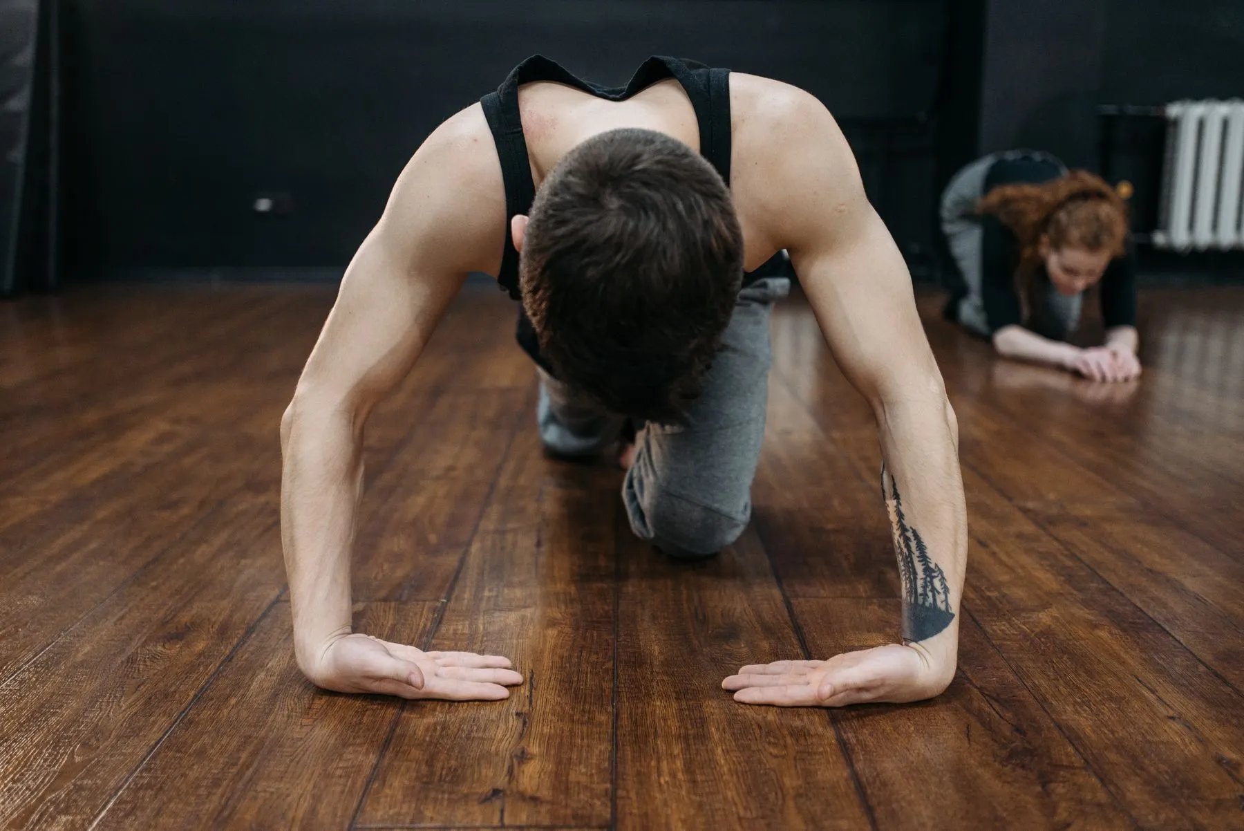 A man on his hands and knees on a wooden floor, stretching his back as part of a floor routine to decompress the spine