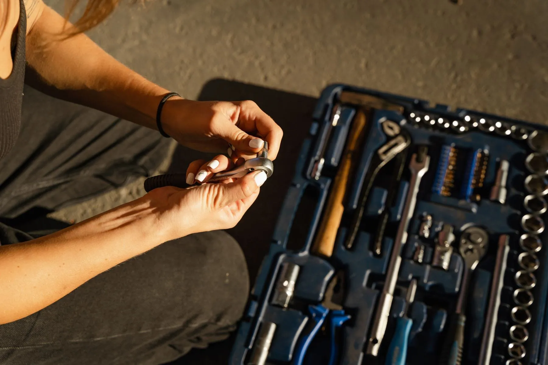 Hands holding a ratchet wrench beside an open toolbox loaded with wrenches, sockets and screwdrivers