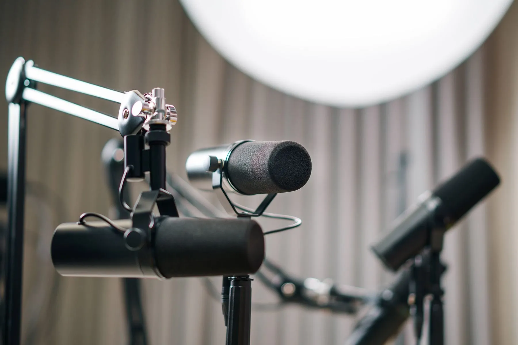 A close-up of podcast studio microphones on boom arms with a softbox light glowing in the background