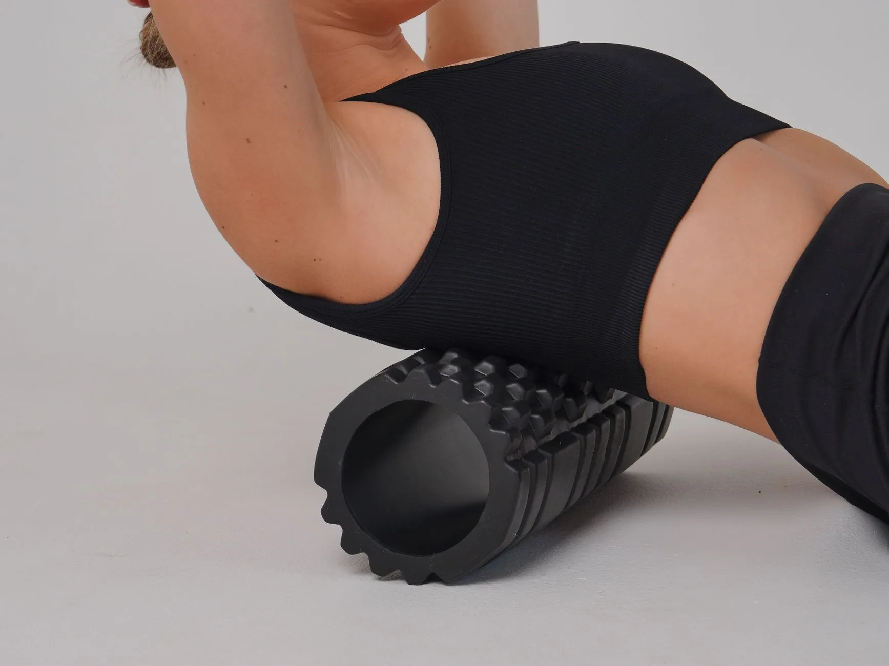 A woman arching her mid-back backward over a black foam roller, the same backward bend a mini inversion table puts you in