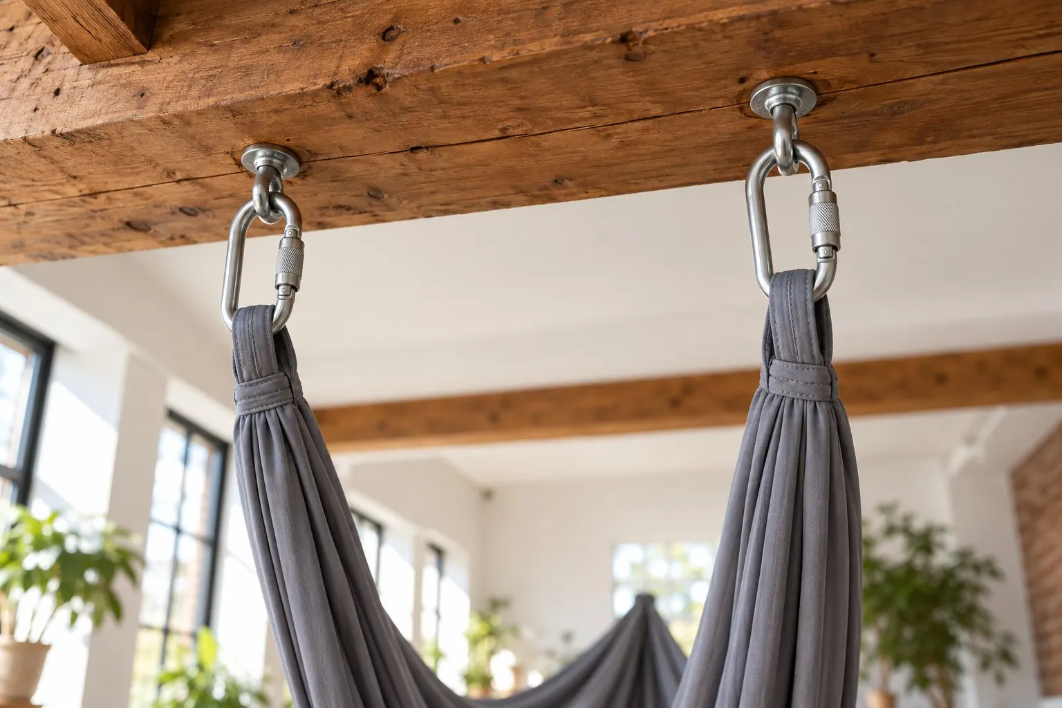 Yoga trapeze straps clipped with carabiners to a heavy exposed wooden ceiling beam