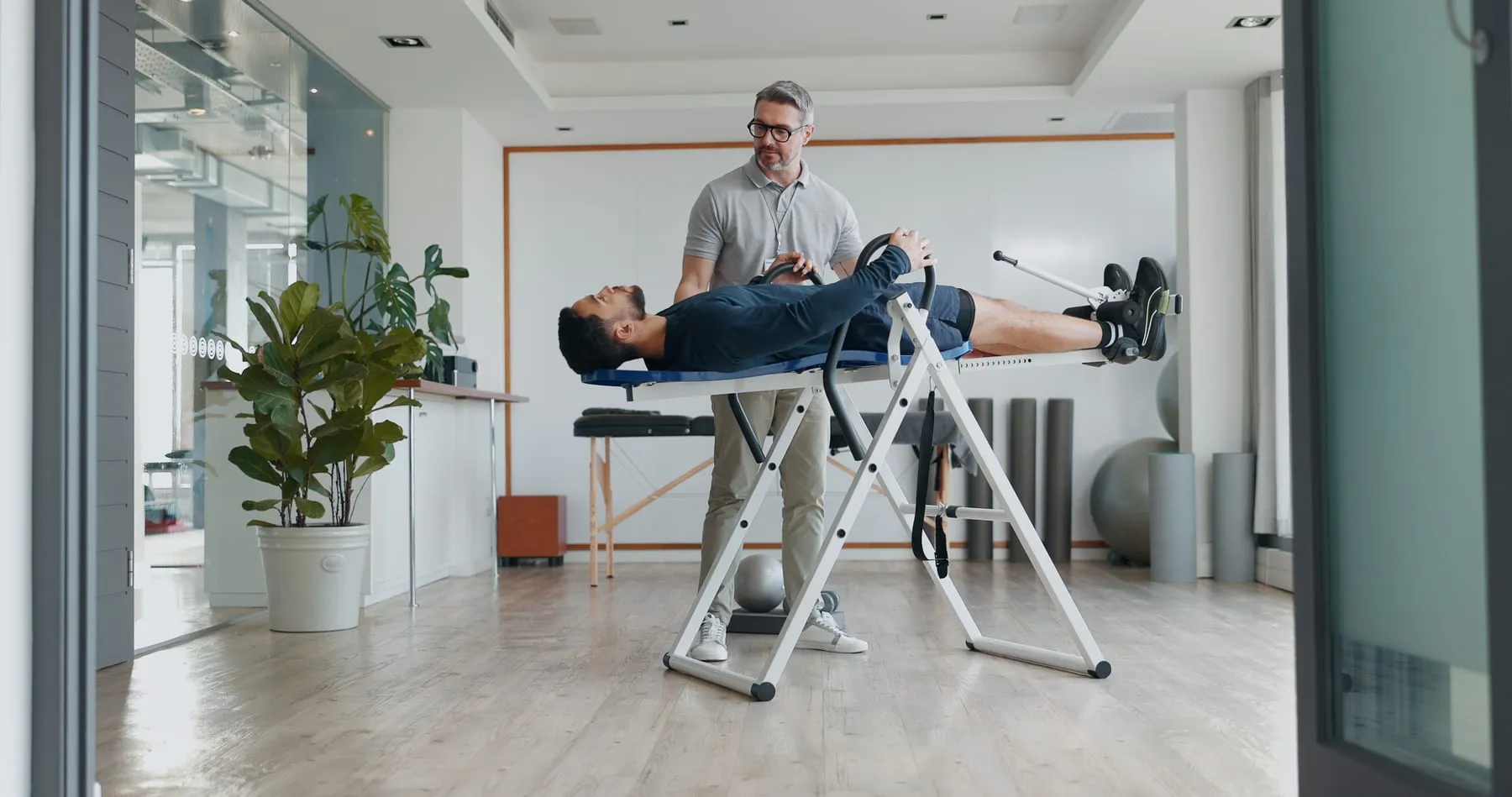 A practitioner standing beside a man lying on an inversion table in a clinic
