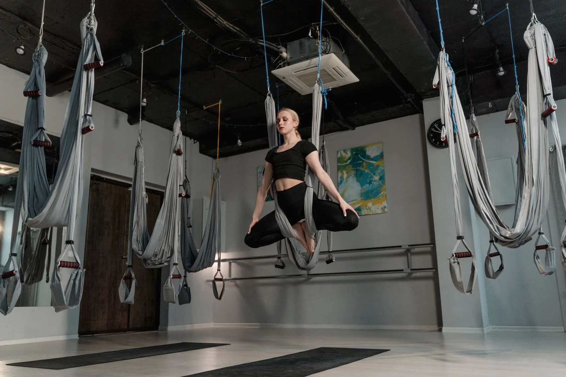 A woman in a supported pose inside a fabric yoga trapeze hanging from a studio ceiling rigged with several other swings